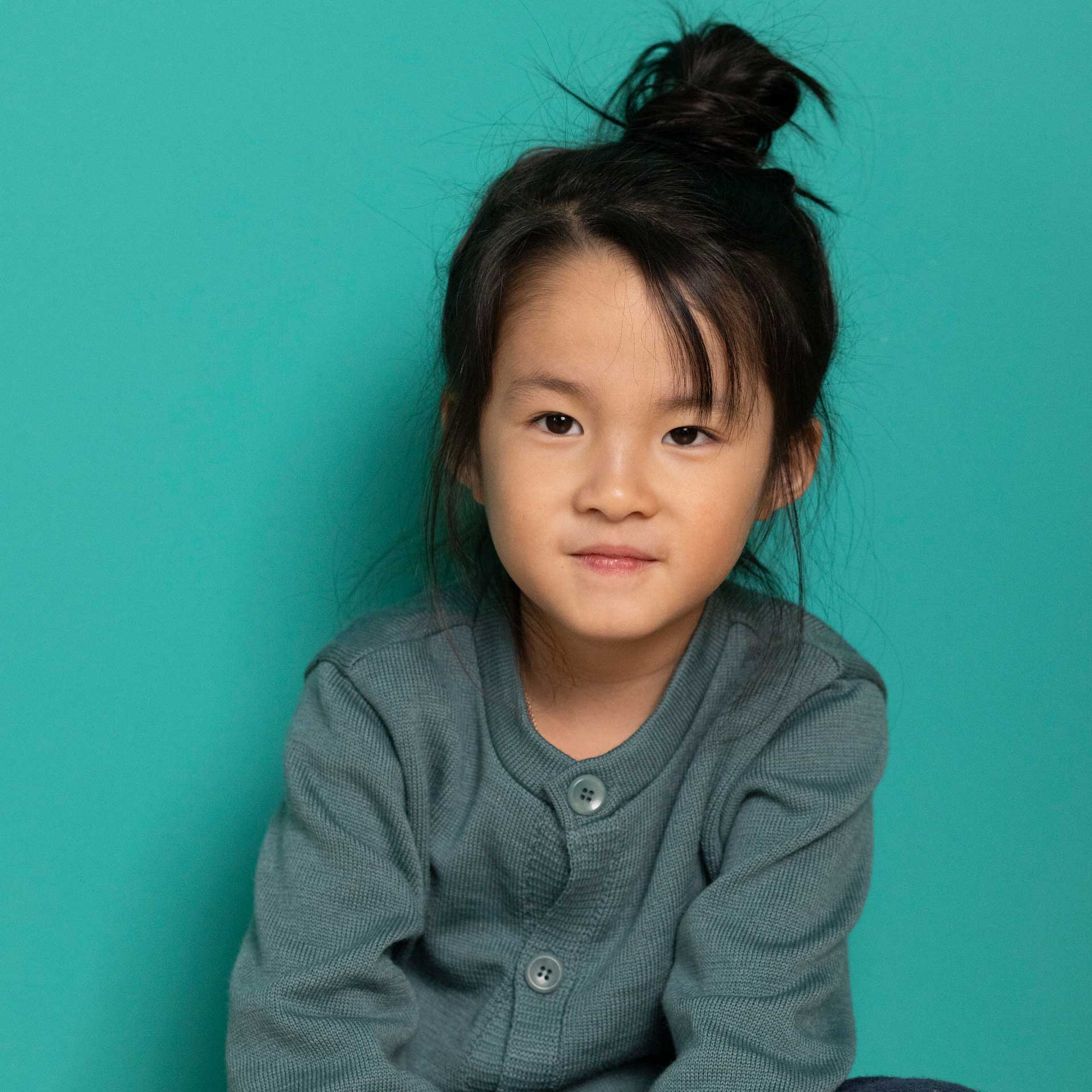 Asiatisches Mädchen mit Messy Bun in disana Strick-Jacke in Eukalyptus vor wassergrünem Studio-Hintergrund