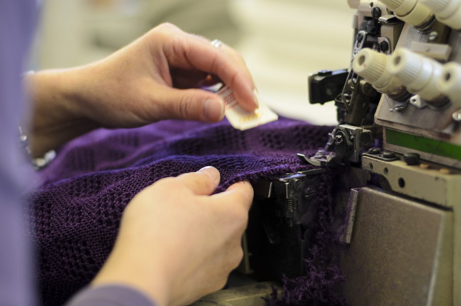 Close Up, es wird von Hand eine Overlock-Naht an einer disana Woll-Babydecke in Pflaume angebracht Strick aus Bio-Merinowolle