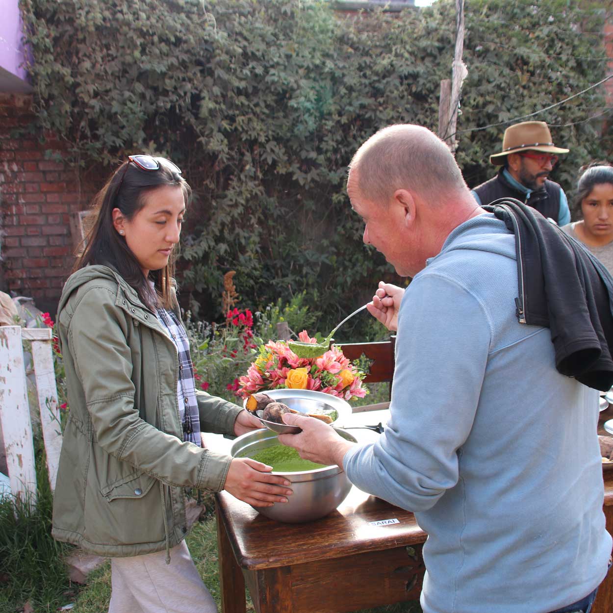 Essensaugabe im Garten der Casa Mantay, Cusco Peru: Elmar Sautter füllt aus einer Schüssel eine grüne Speise in seinen Teller