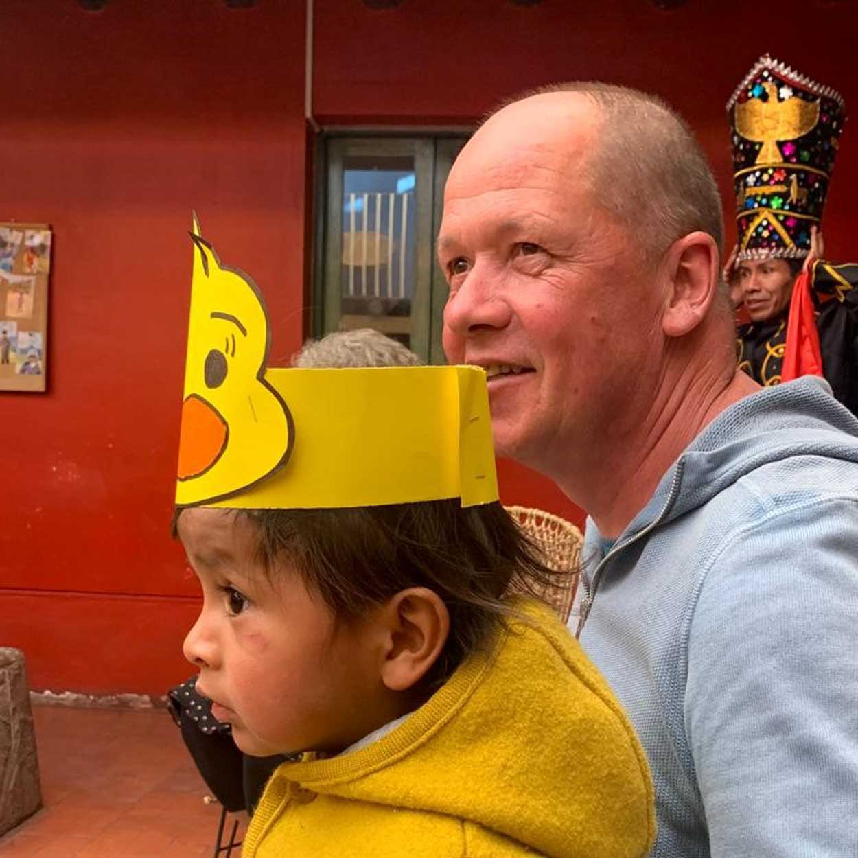 Casa Mantay, Cusco, Peru: Profil eines Kindes in disana Walk-Overall in Curry neben lächelndem Elmar Sautter vor roter Wand.