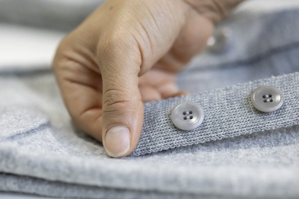 Eine Hand hält einen grauen disana Strick-Träger an dem zwei farblich passende Steinnussknöpfe angenäht sind