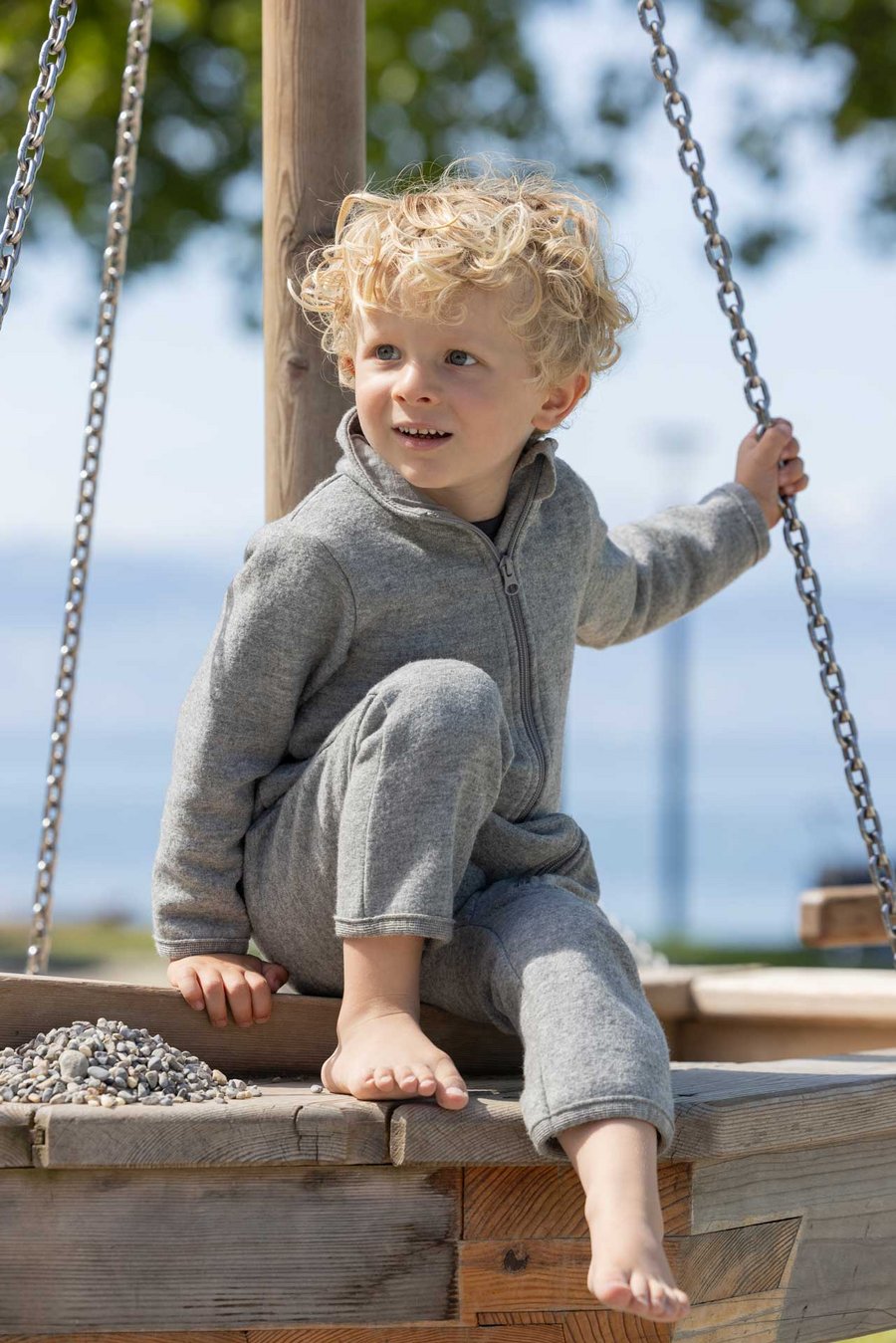 Kind im grauen disana Walk-Anzug auf Spielplatz am Seeufer, Wollwalk in Sommerqualität, 260g/m² aus Bio-Merinowolle