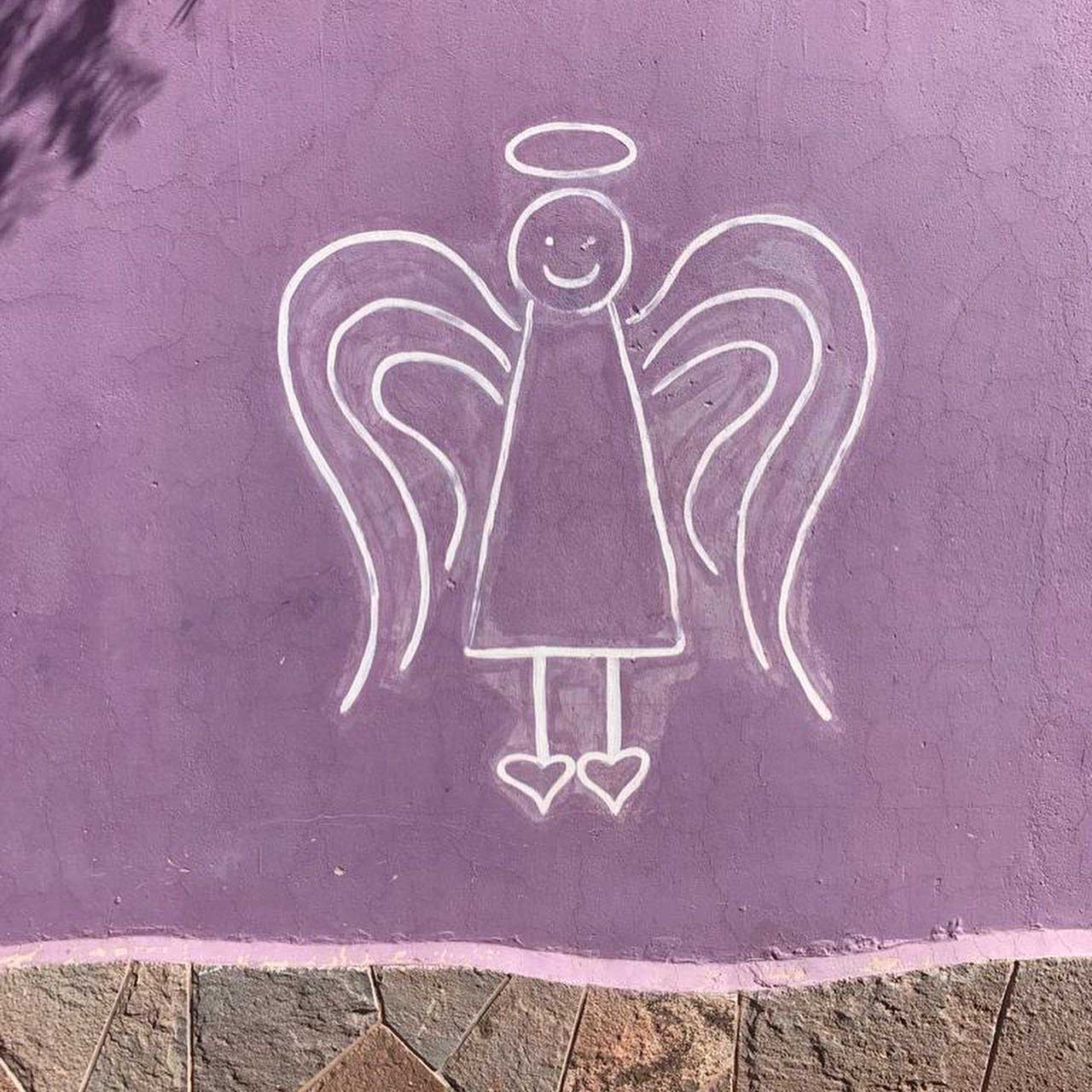 Weiße Strichzeichnung eines lächelnden Engels mit Flügeln, Heiligenschein und Herz-Füßen auf einer lila Wand.