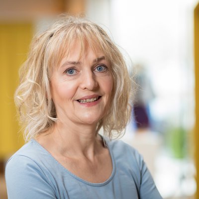 Portrait von Sonja Wahl, Buchhalterin der disana GmbH & Co. KG, im blauen Shirt, lächelnd vor unscharfem Hintergrund
