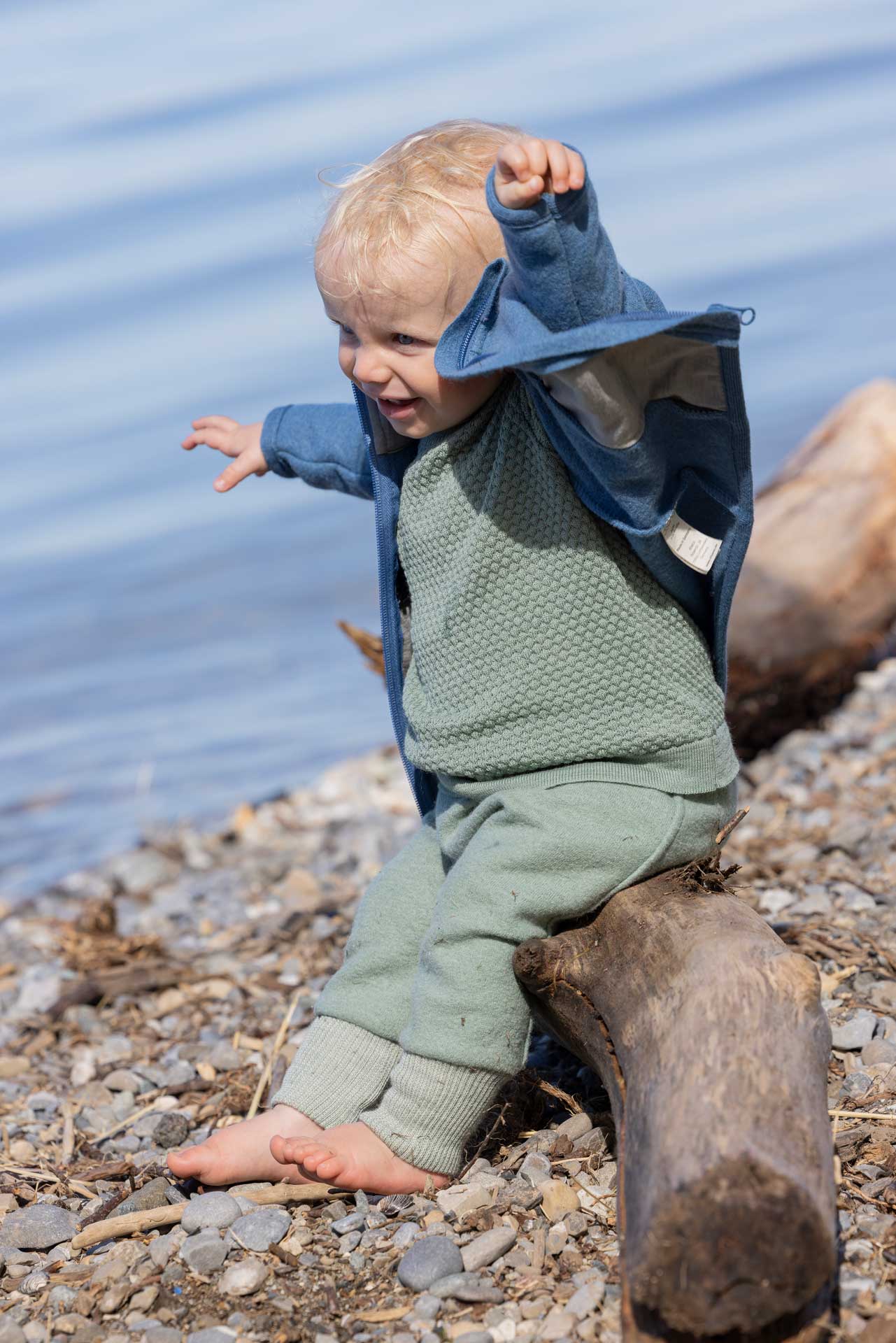 Toddler in a dove blue disana Zipper Jacket and jade bloomers by a lake