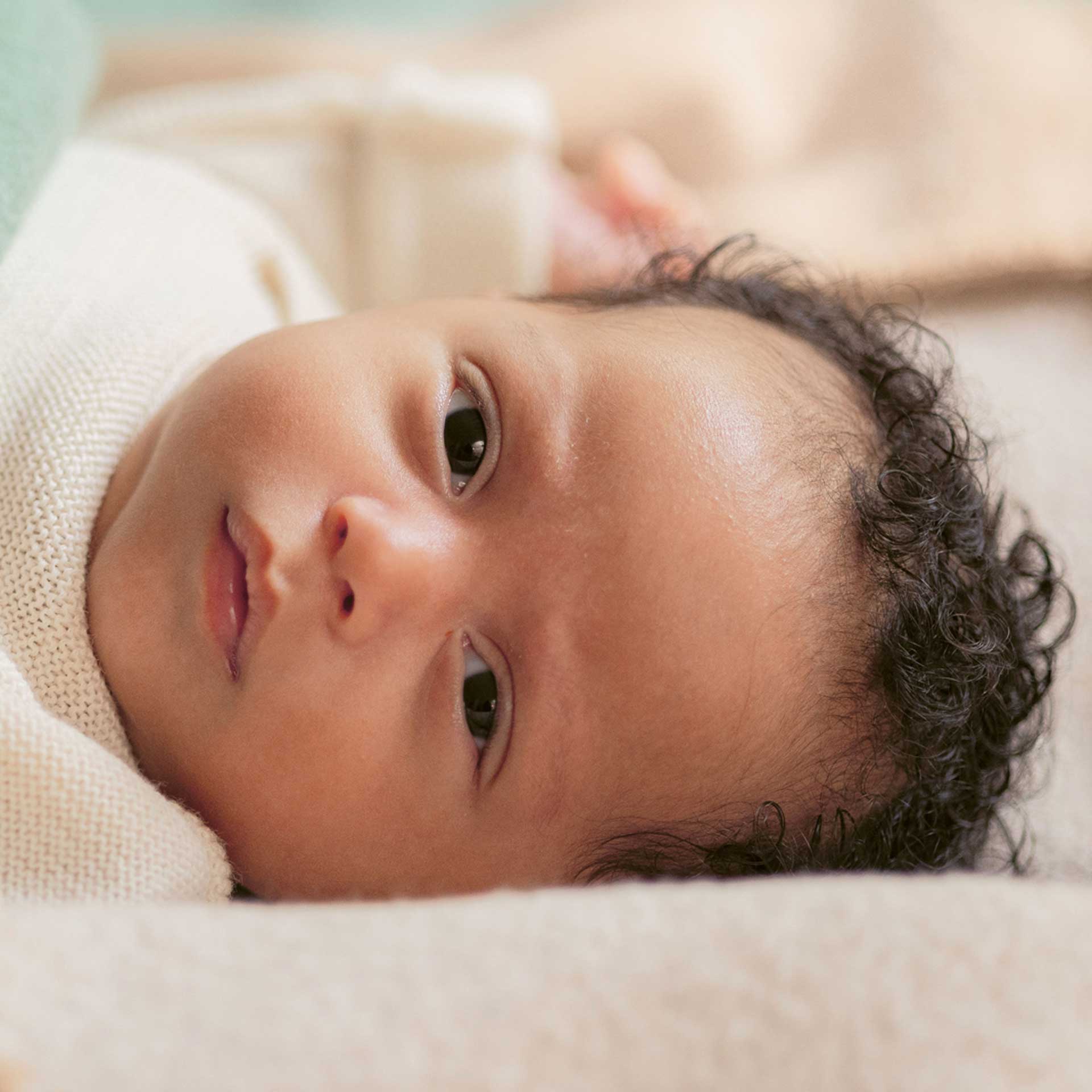 Close Up eines liegenden Baby mit hellbraunem Hautton - Kleidung und Hintergrund in naturweißen Tönen