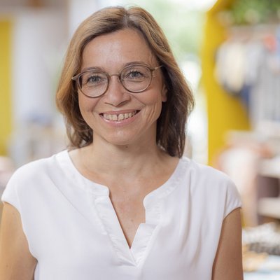 Portrait von Elisabeth Courbet, Sachbearbeiterin der disana GmbH & Co. KG im weißen Shirt lächelnd vor unscharfem Hintergrund