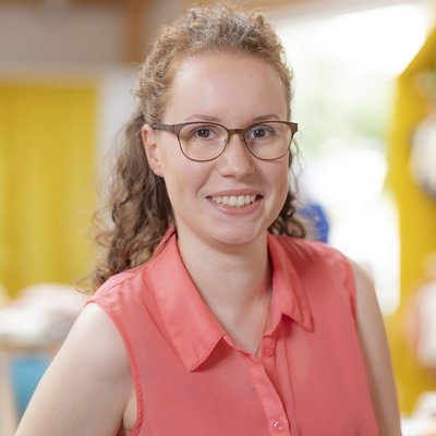 Portrait von Doreen Böbel, Sachbearbeiterin der disana GmbH & Co. KG, in orangener Bluse, lächelnd vor unscharfem Hintergrund